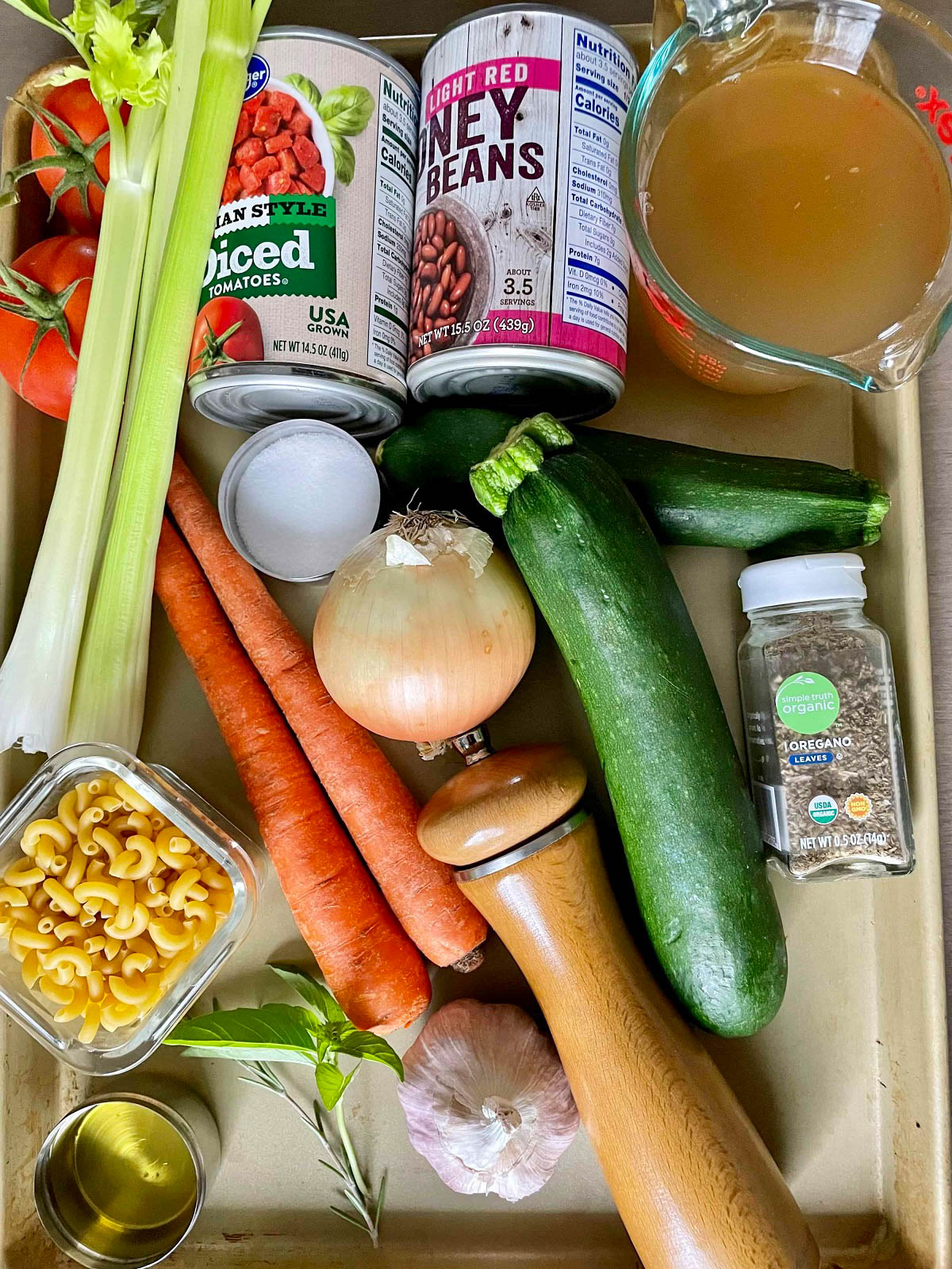 Ingredients_Minestrone-Soup on a metal tray - celery, tomatoes, broth, canned beans, spices, zucchini, onion, garlic, and carrots.