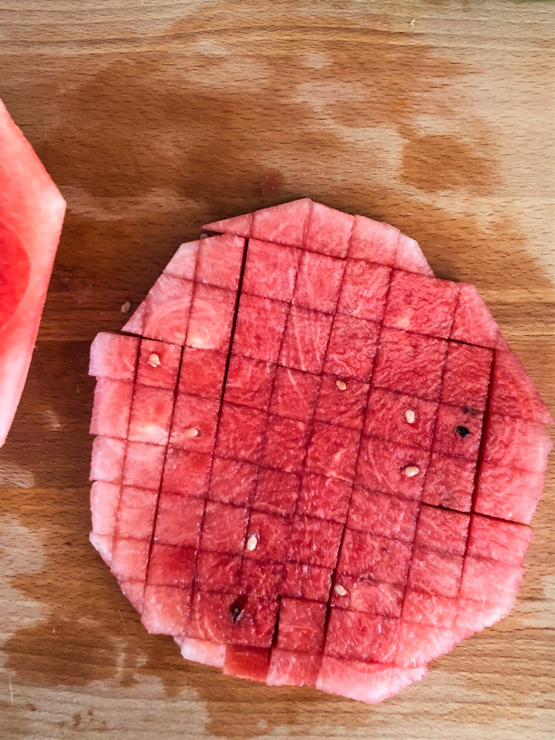 A disc of watermelon diced into small cubes on a wooden chopping block.