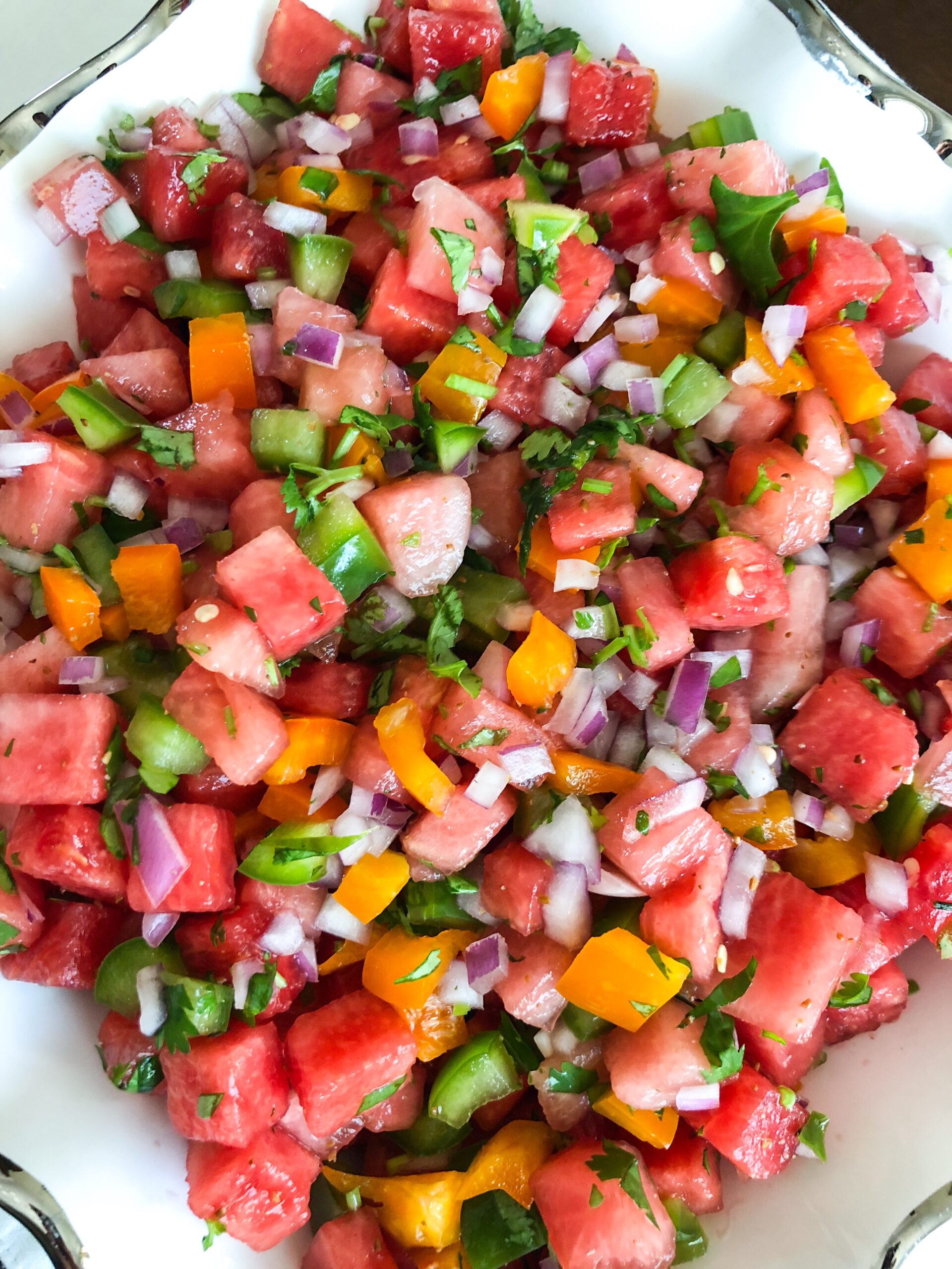 Watermelon jalapeno salsa with bell peppers and onions served in a white ceramic dish, garnished with chopped cilantro.