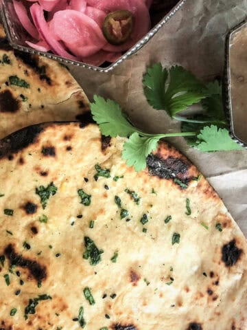 Garlic Naan bread with herbs, pickled onions, and chutney, served on a rustic surface. Ideal for Indian meals.