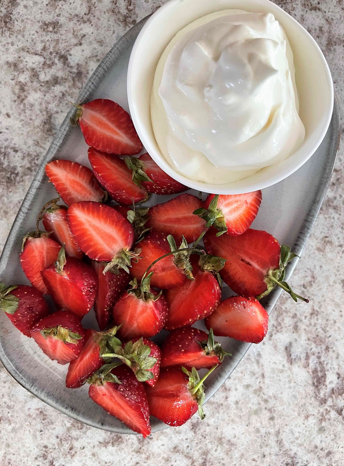a metal tray containing sliced fresh strawberries next to a container of whipped cream.