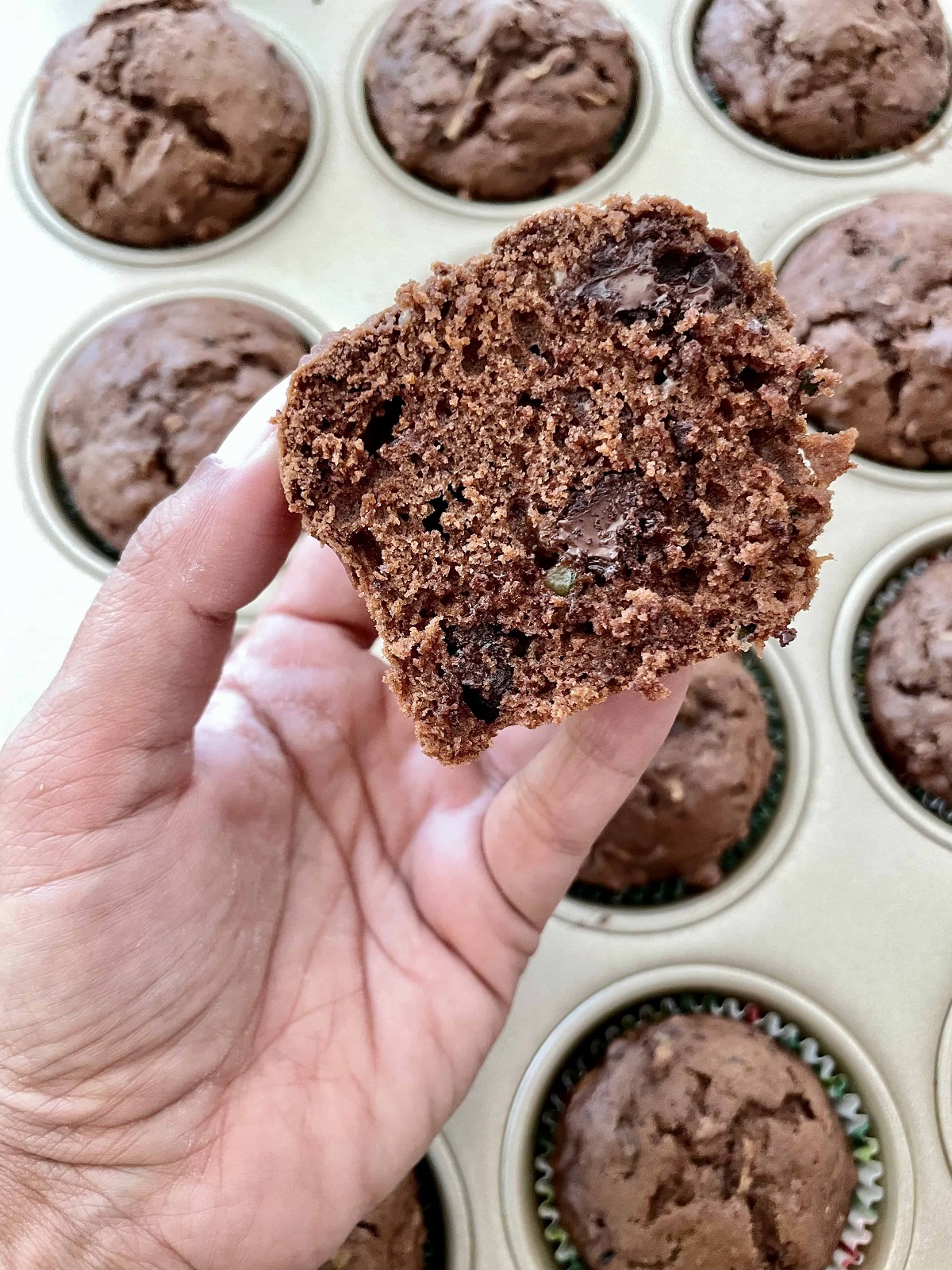 A hand holding a chocolate chip zucchini muffin that has been sliced in half