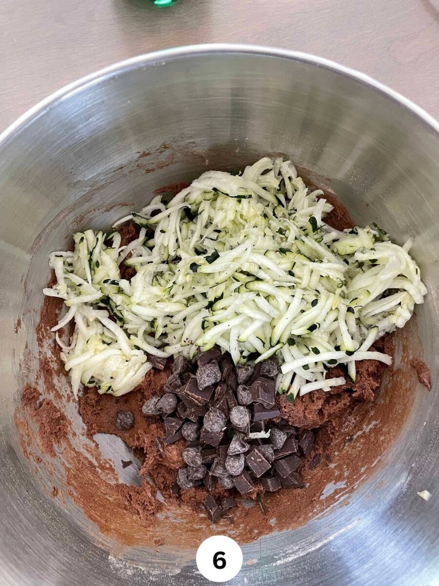 shredded zucchini and chocolate chips with chocolate muffin batter in a steel mixing bowl.