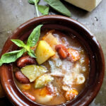 Minestrone soup served in a ceramic bowl garnished with grated parmesan and fresh basil sprig