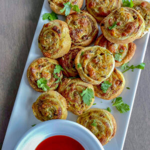 Savory appetizer pinwheels served on a white ceramic platter with a bowl of ketchup