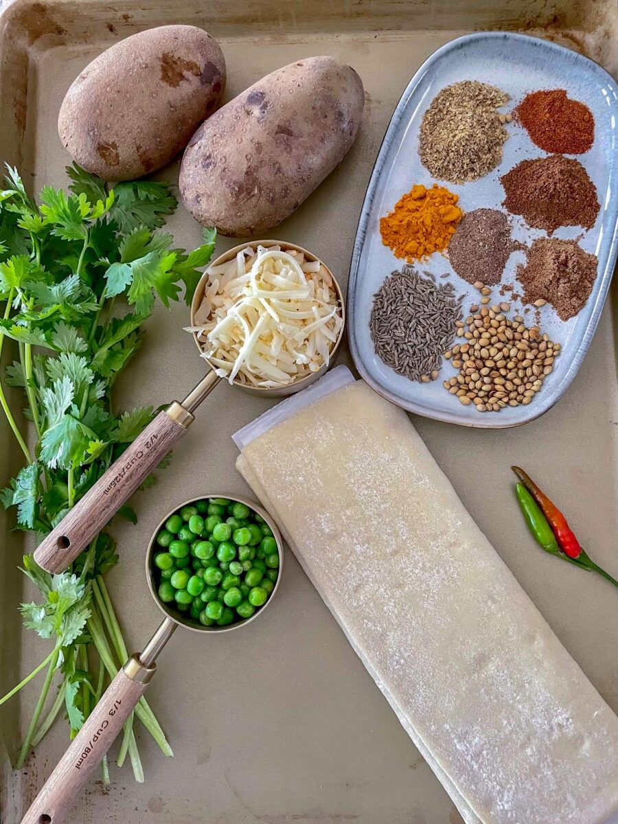 Ingredients for Savory Appetizer Pinwheels on a metal tray - potatoes, cheese, spices, cilantro, peas, puff pastry sheet and green chili.
