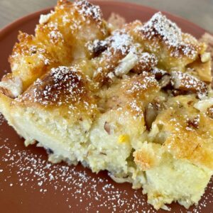 Indian Bread Pudding dusted with powdered sugar, served on a terracotta plate.