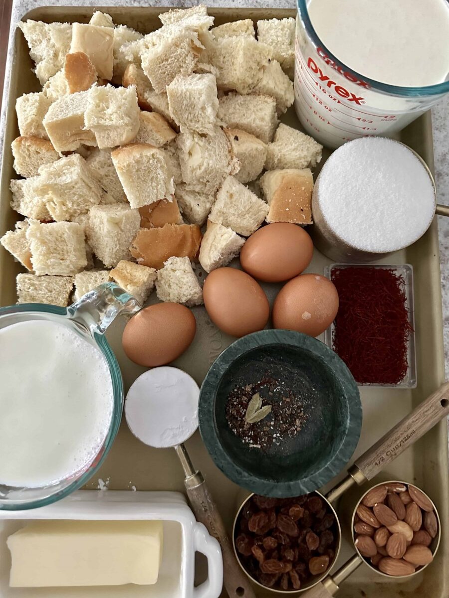 Ingredients to make Indian Bread pudding on a metal tray including Bread pieces, milk, cardamom, saffron, and eggs.