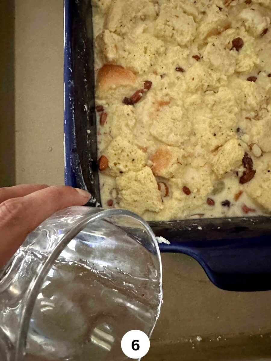 Pouring water in a cookie sheet that has the baking dish with Indian Bread Pudding ingredients ready to be baked.