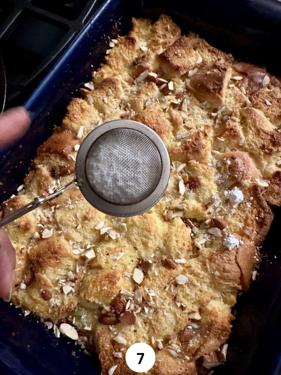 Dusting baked Indian bread pudding with powdered sugar in a small steel sieve.