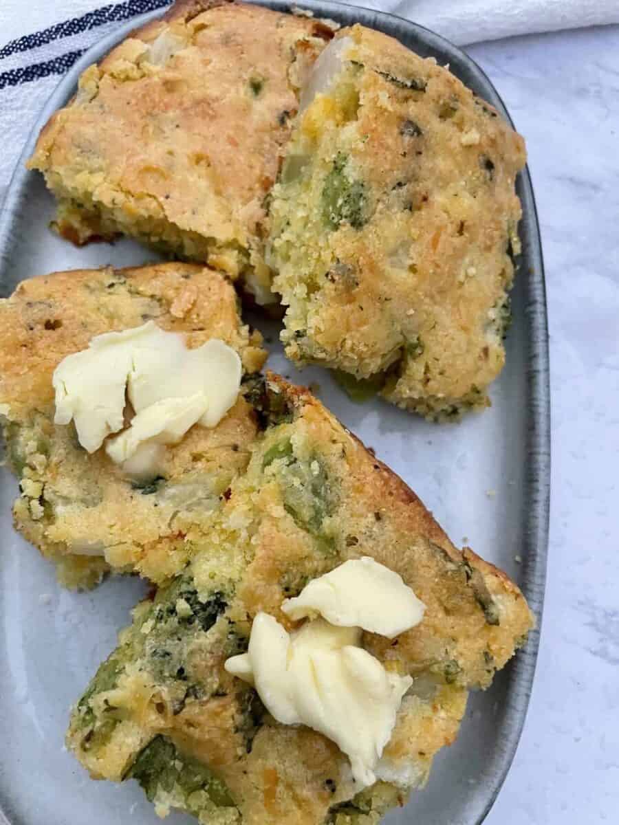 Slices of Broccoli Cheddar Cornbread with butter on a grey ceramic plate.