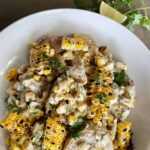 Charred Corn and smashed potatoes dressed with a yogurt based sauce and garnished with chopped cilantro in a white bowl.