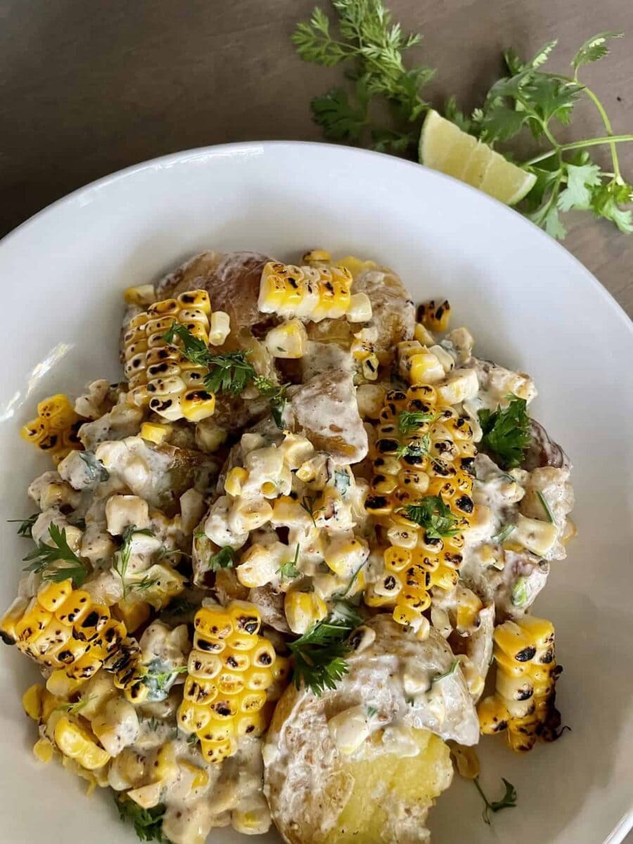 Charred Corn and smashed potatoes dressed with a yogurt based sauce and garnished with chopped cilantro in a white bowl.