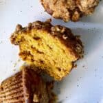 Halved Spiced Pumpkin Muffins with Pecan Crumb Topping on a white ceramic plate with some crumbs.