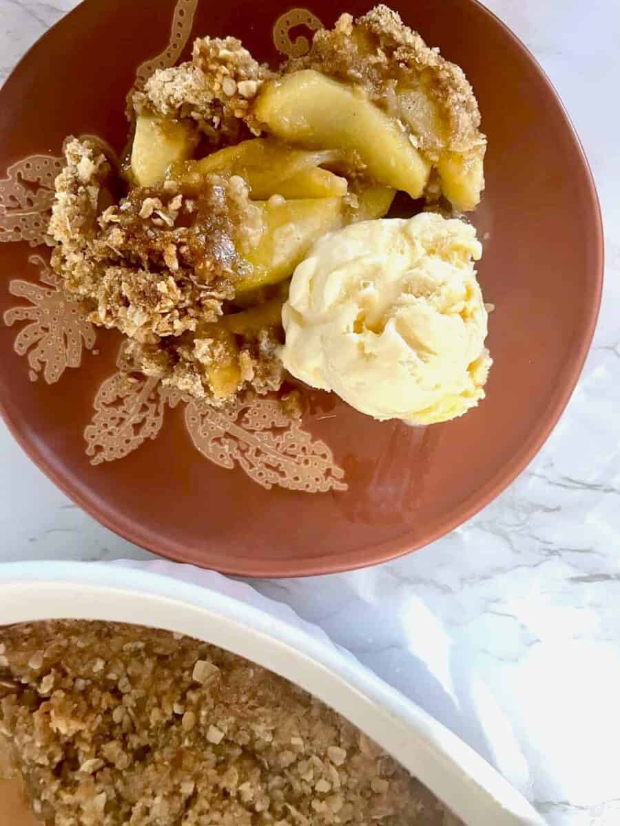Apple crisp served on a terracotta plate along with a scoop of vanilla ice cream.