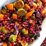 Roasted brussel sprouts, pomegranate seeds, red onions, and butternut squash in a white ceramic serving platter.