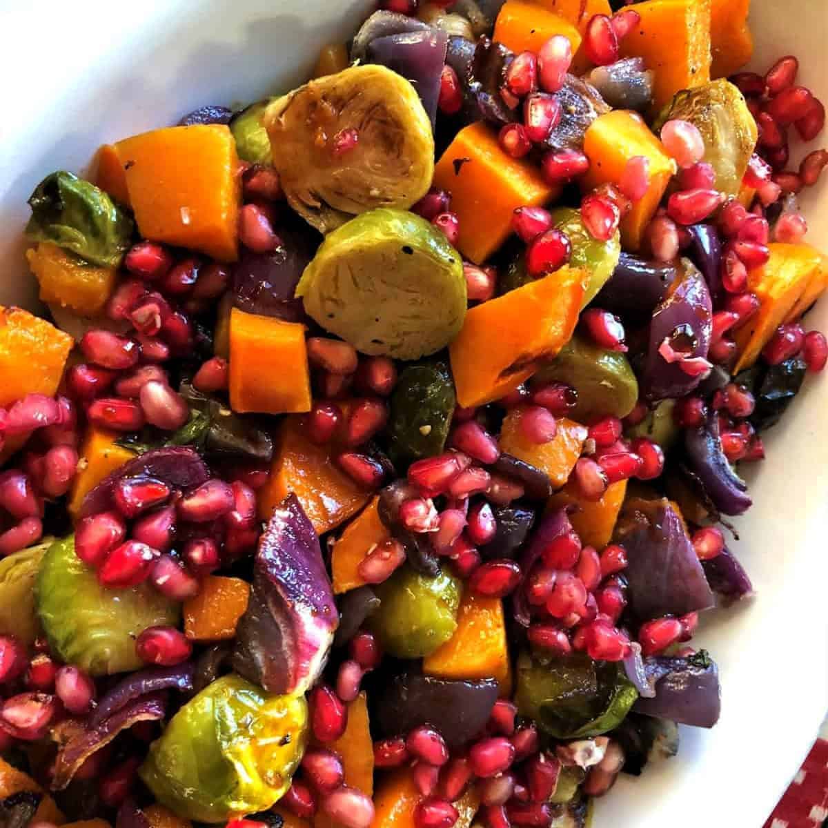 Roasted brussel sprouts, pomegranate seeds, red onions, and butternut squash in a white ceramic serving platter.