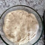 Whole wheat flour dough in a glass bowl on a kitchen counter.