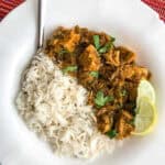 Coriander Chicken Curry garnished with chopped cilantro served with basmati rice and two slivers of lemon in a white ceramic plate.