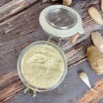 Ginger Garlic paste in a small mason jar with fresh garlic and ginger in the background on a rustic wooden table.