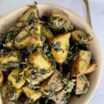 Aloo Methi in a beige ceramic bowl on a white marble background with a golden spoon in the top right corner.