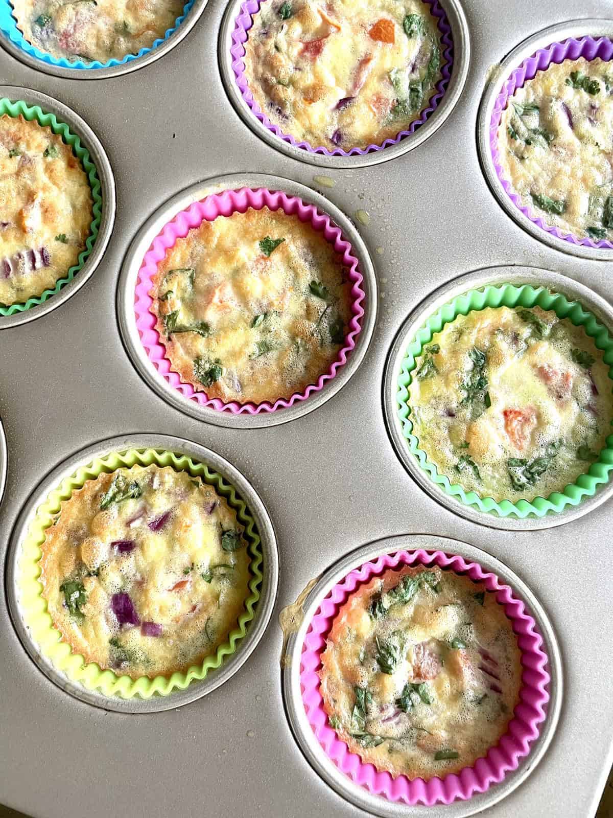 Baked egg bite with onion and tomato in a silicon liners lined muffin pan.