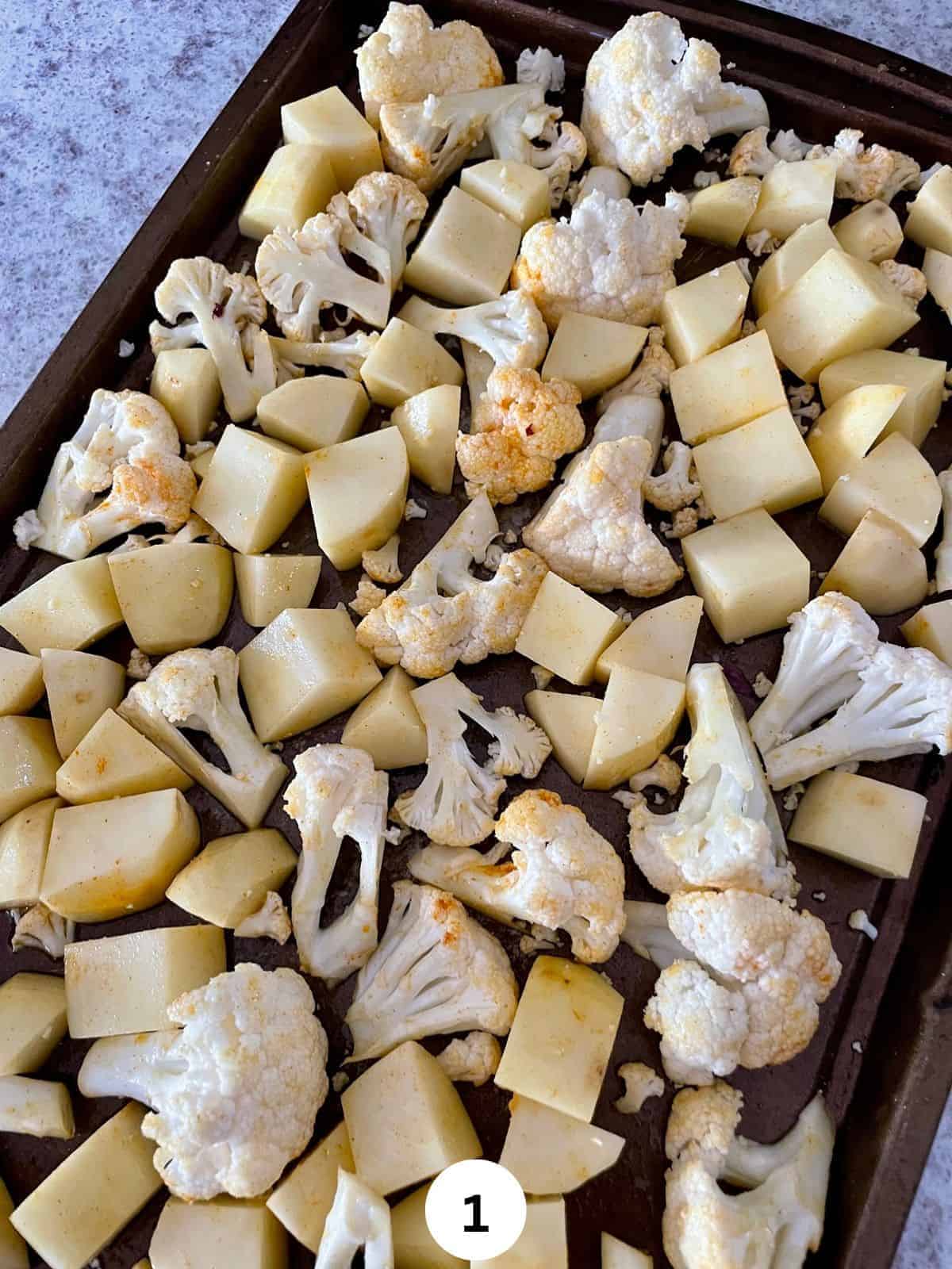 Cubed potatoes and cauliflower florets with turmeric on a cookie sheet.