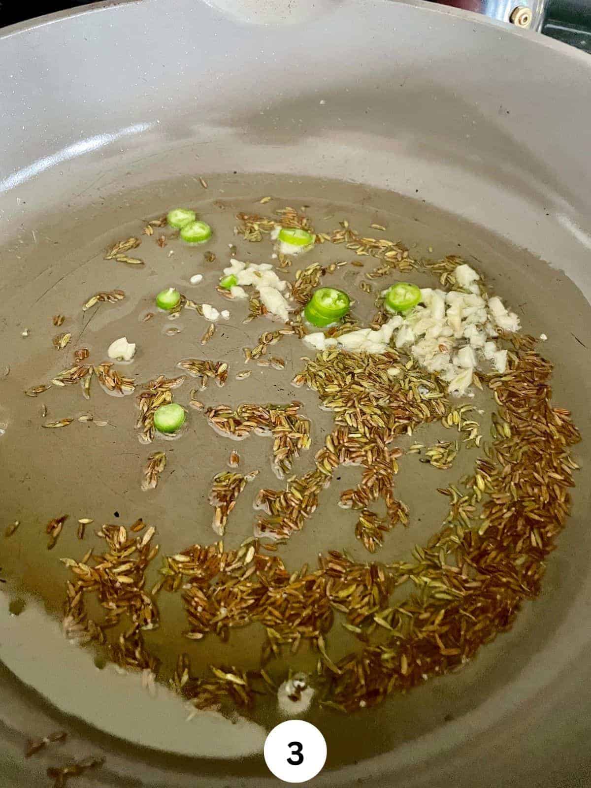 Grated garlic and chopped green chili in a saute pan with oil and cumin seeds.