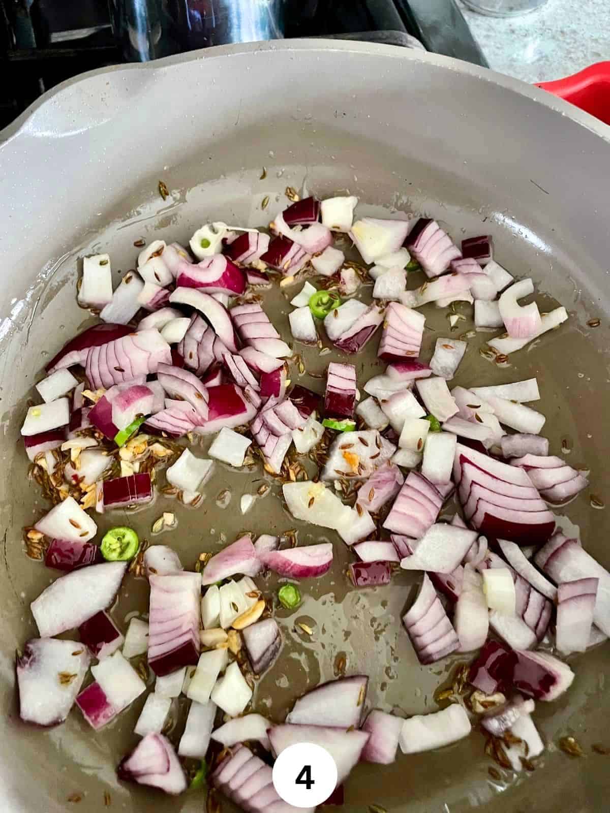 Chopped onions and green chili in a saute pan with oil and cumin seeds.