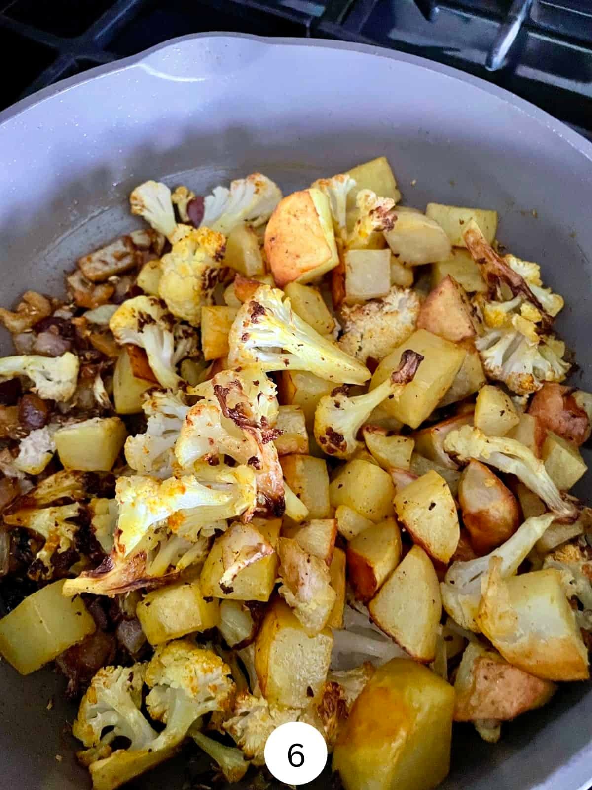 Cooked Potatoes and cauliflower with Indian spices in a ceramic saute pan.