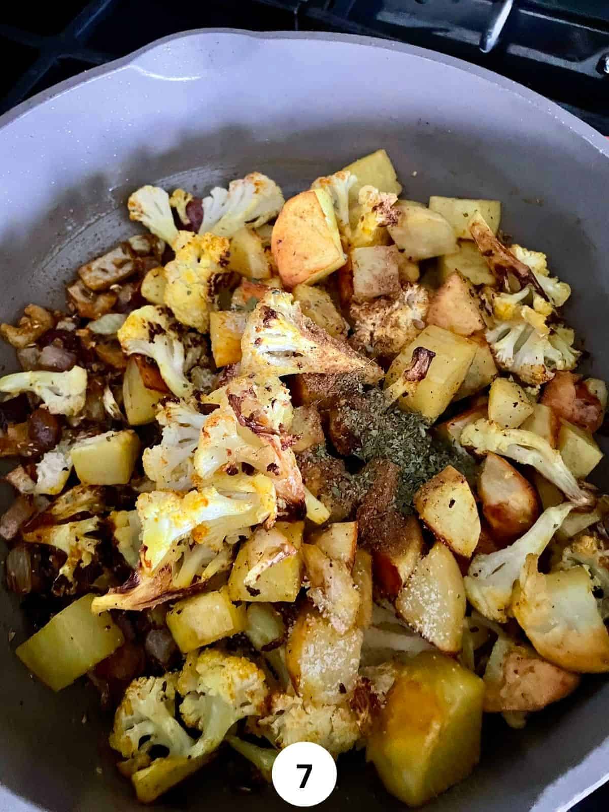 Cooked Potatoes and cauliflower with Indian spices in a ceramic saute pan sprinkled with garam masala and kasoori methi.