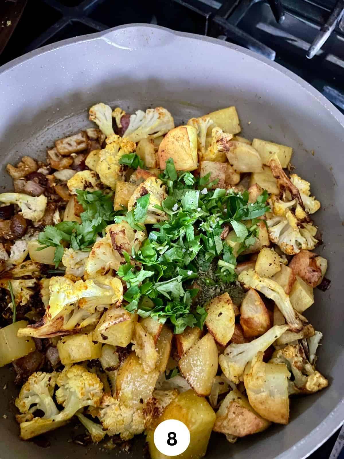 Potatoes and cauliflower in a grey ceramic saute pan garnished with chopped cilantro.