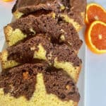 A marbled chocolate and orange loaf cake sliced and arranged on a white rectangular ceramic platter with slices of orange along the sides of the platter for garnish.