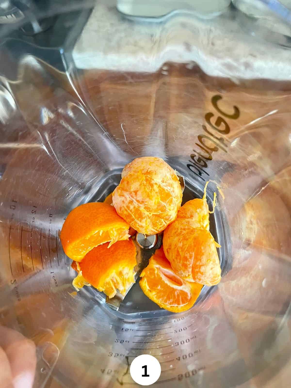 Peeled and unpeeled oranges in a blender jar.