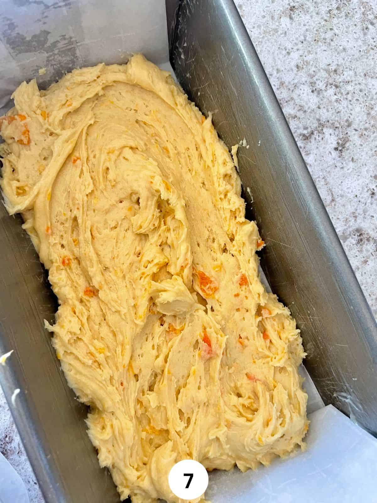 Orange cake batter in a parchment lined metallic loaf pan.