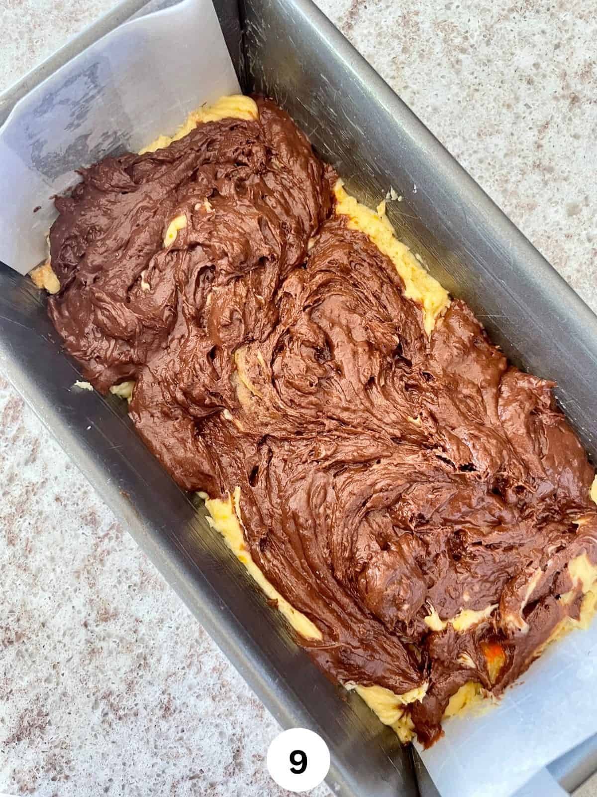 Chocolate and orange batter swirled together in a parchment lined metallic loaf pan.
