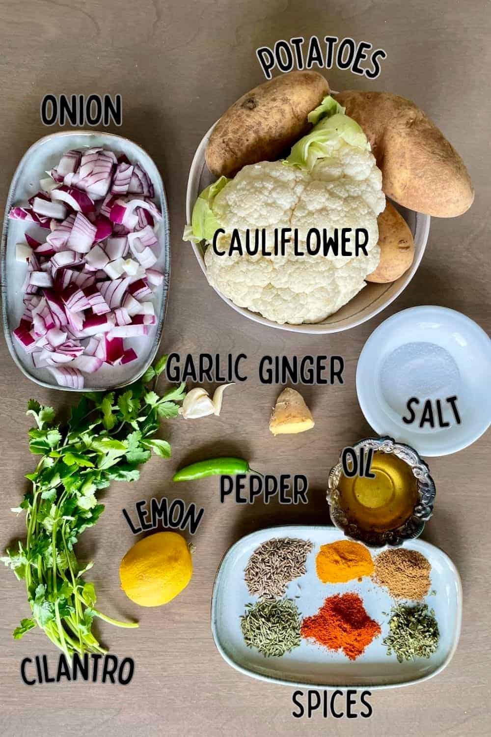Ingredients to make oven roasted aloo gobi on a brown wooden background.
