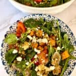 A lentil and roasted vegetable salad with spinach and feta cheese served in a white and blue ceramic bowl against a white marbled background.