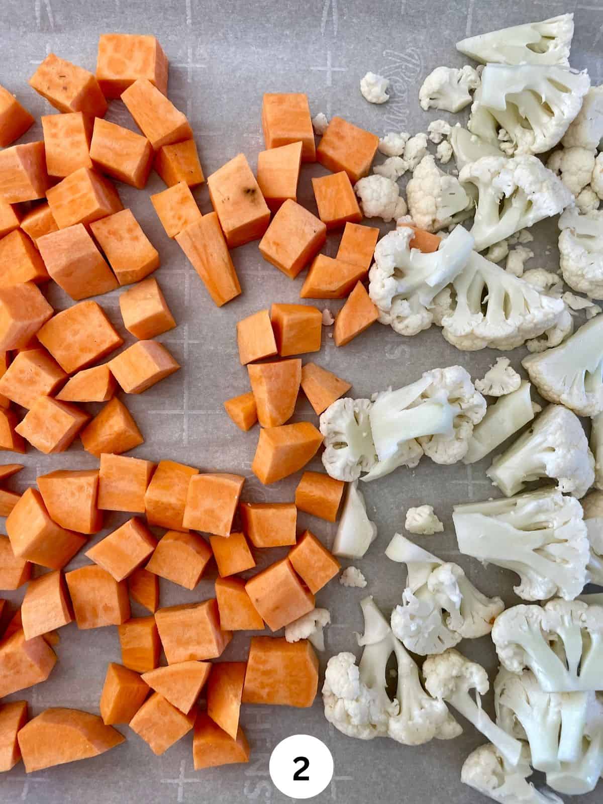 Cubed sweet potato and cauliflower florets on a parchment lined cookie sheet.