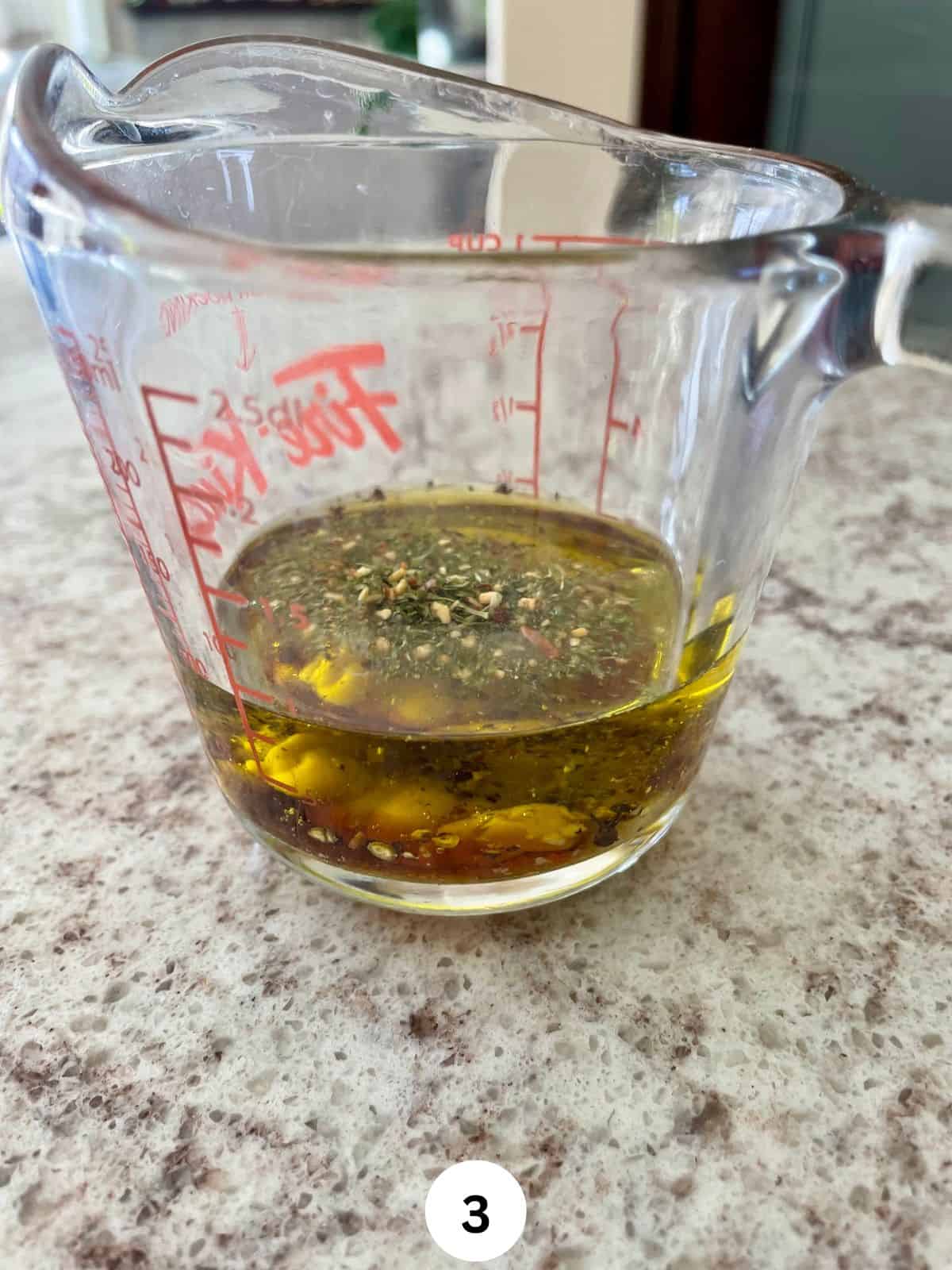 Olive oil and greek seasoning in a glass measuring cup.
