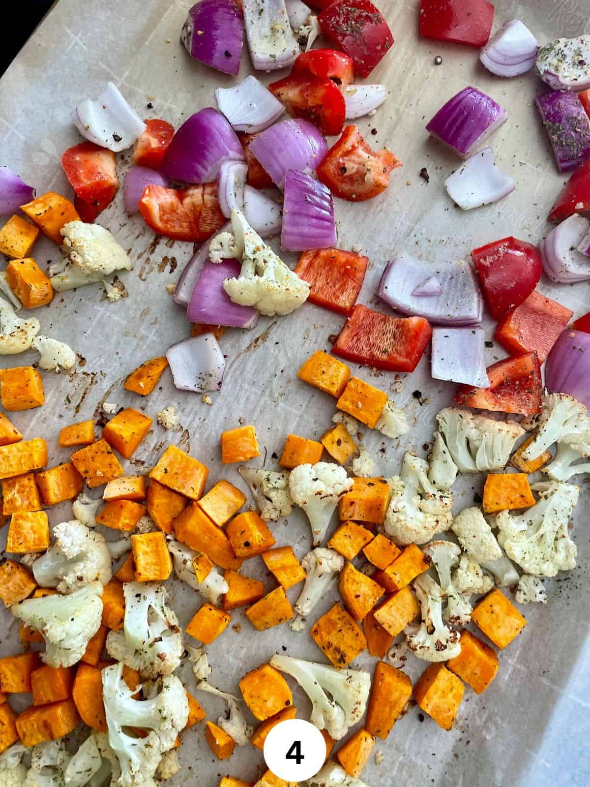 Roasted cubed sweet potato, cauliflower florets and chopped red onions and red bell peppers on a parchment lined cookie sheet.
