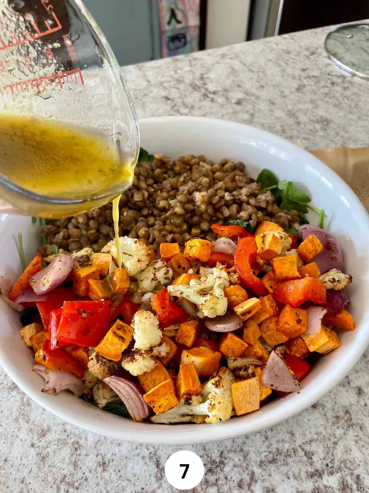 Pouring dressing into a bowl with roasted vegetables and cooked brown lentils.
