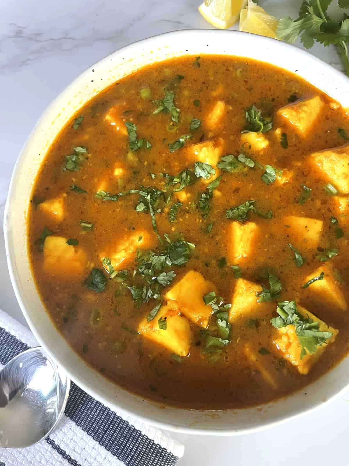 Matar Paneer Curry garnished with chopped cilantro in a white ceramic bowl on a white marble background.
