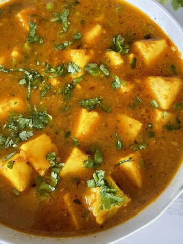 Matar Paneer Curry garnished with chopped cilantro in a white ceramic bowl on a white marble background.