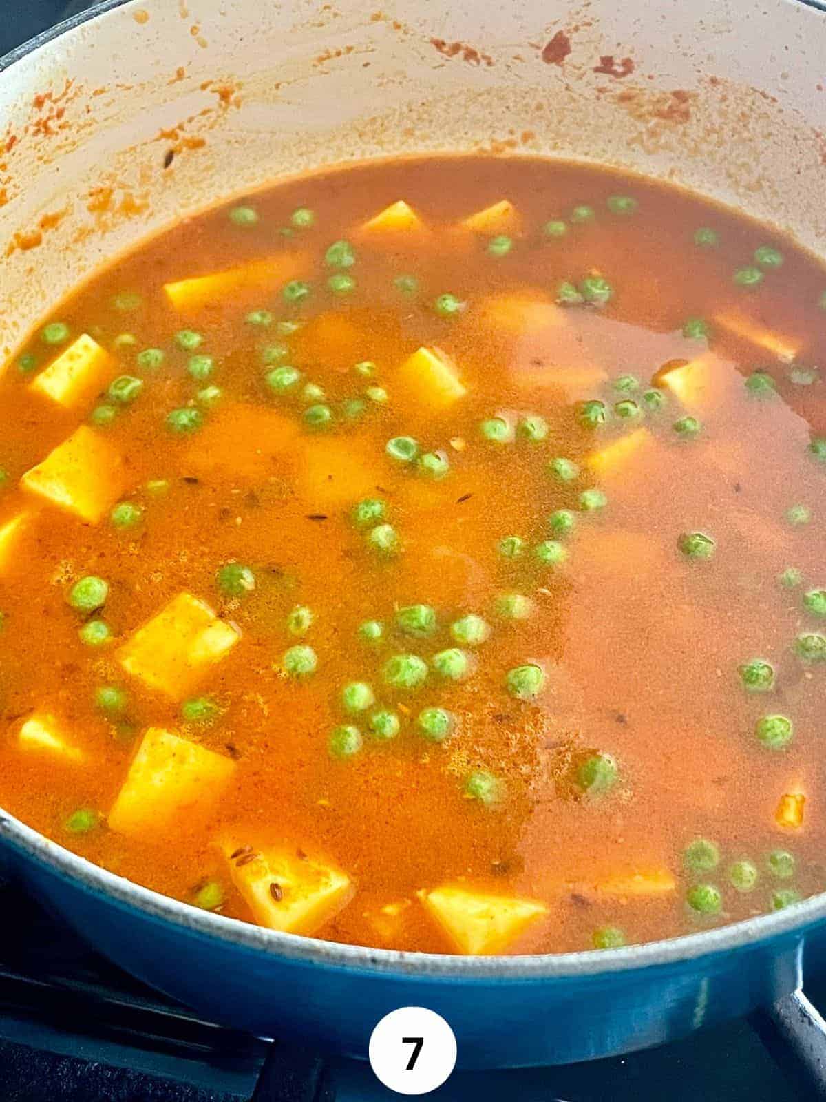 Matar Paneer cooking in a blue enameled cast iron pan with cubed paneer and peas floating in the curry sauce.