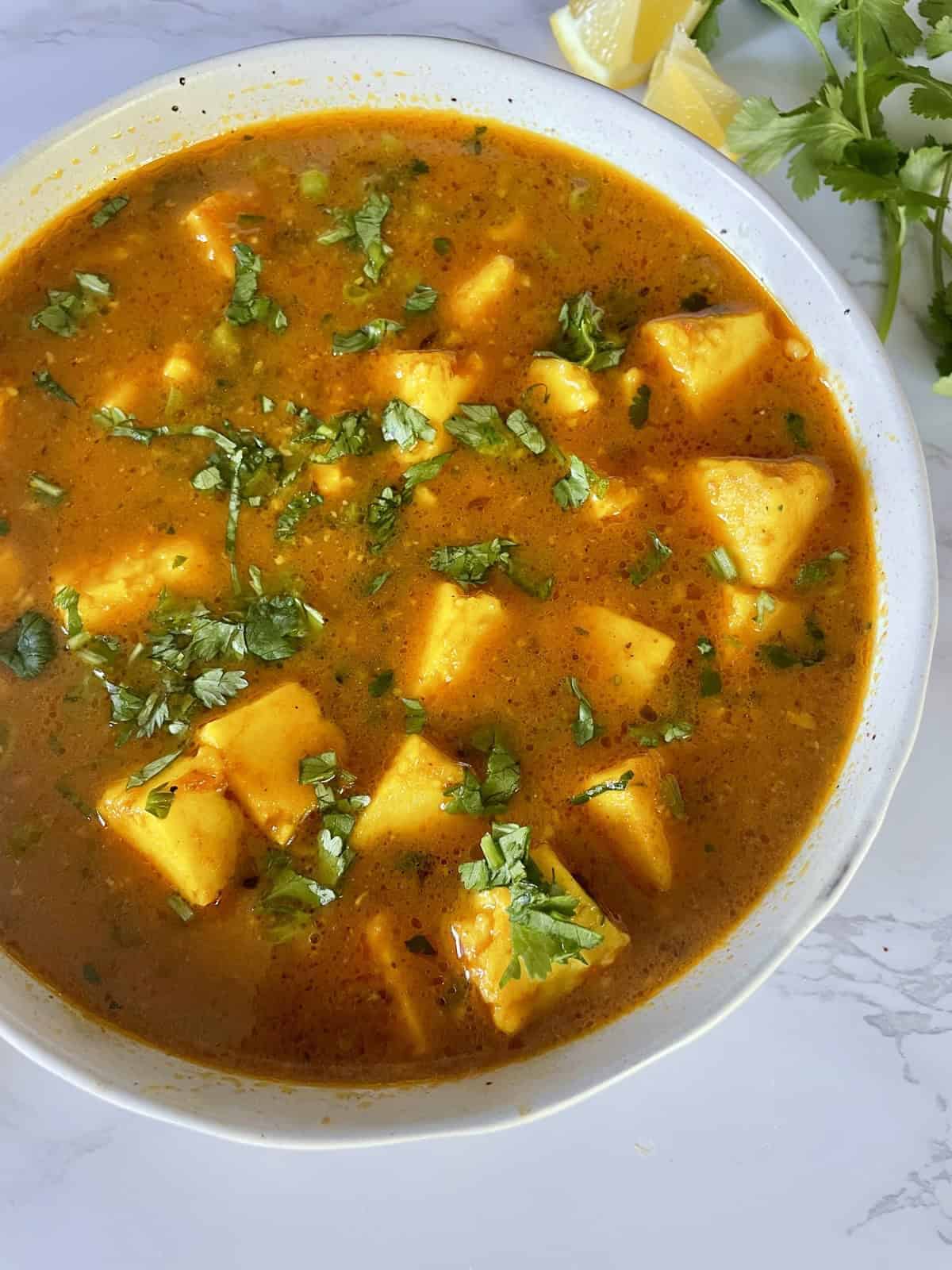 Matar Paneer Curry garnished with chopped cilantro in a white ceramic bowl on a white marble background.
