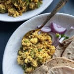 Paneer Bhurji served with rotis and a salad of red onions and green chilis in a speckled white ceramic bowl.