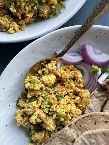 Paneer Bhurji served with rotis and a salad of red onions and green chilis in a speckled white ceramic bowl.