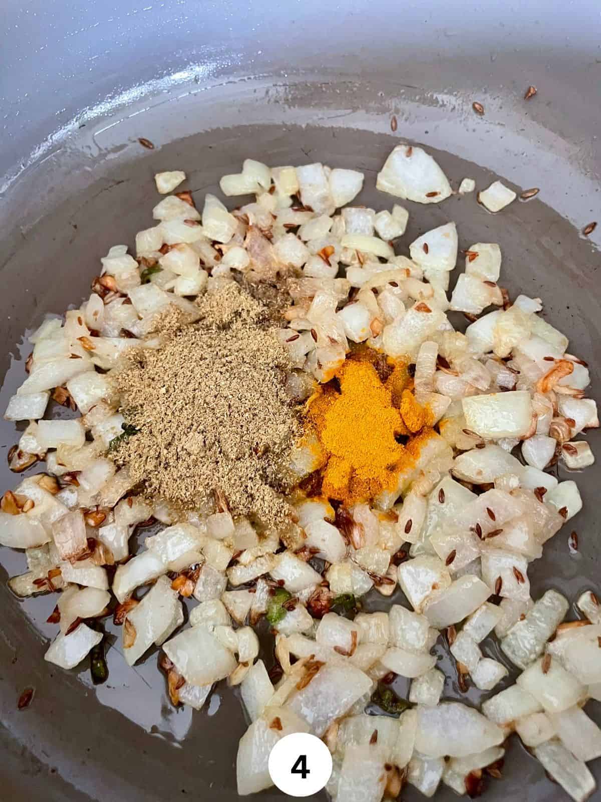 Onion masala with cumin seeds, turmeric and coriander powders in a grey ceramic pan.