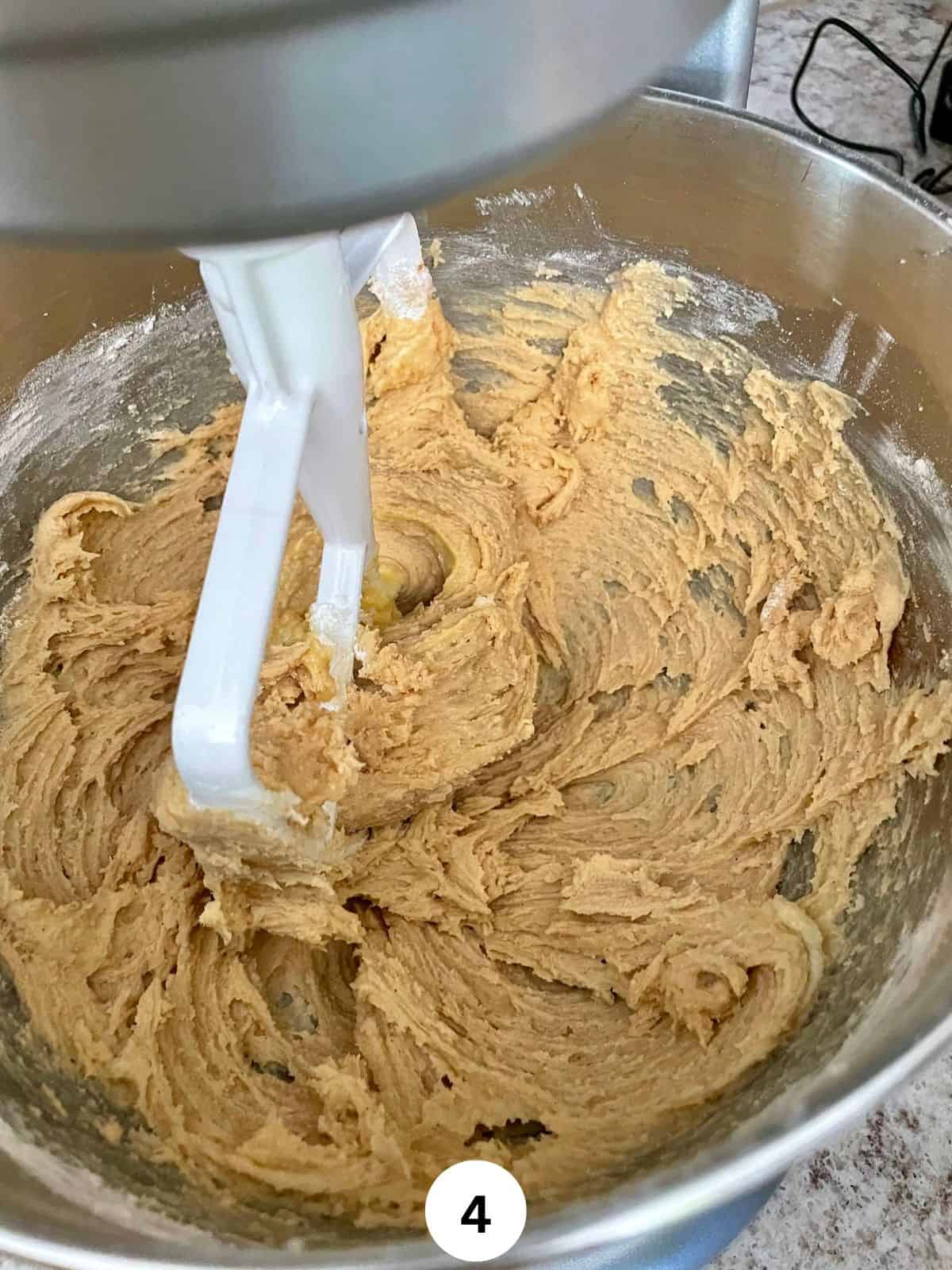 Cake batter in a stainless steel bowl with a stand mixer paddle attachment.